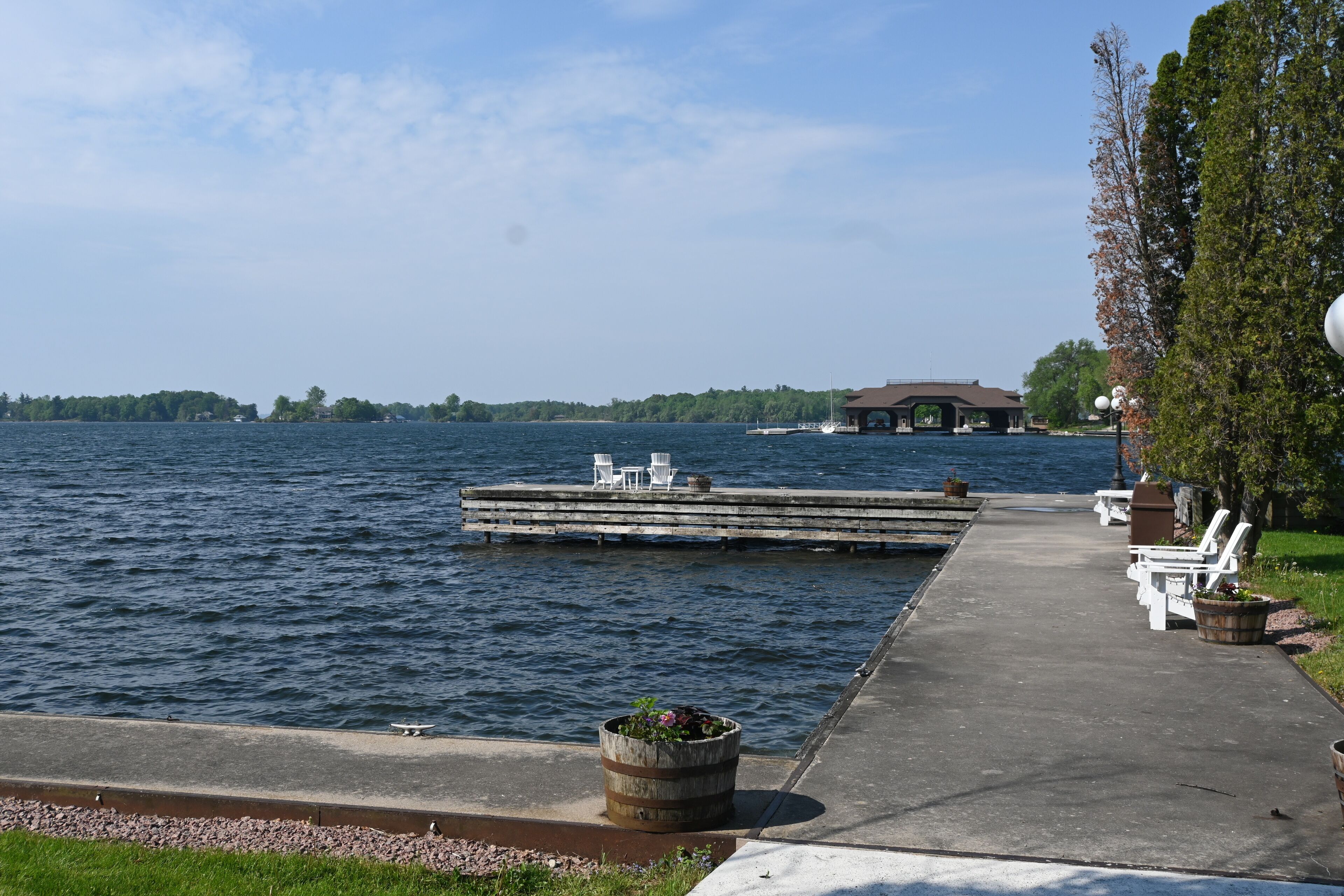 Un muelle junto al lago con sillas blancas y una jardinera de madera cerca del agua.