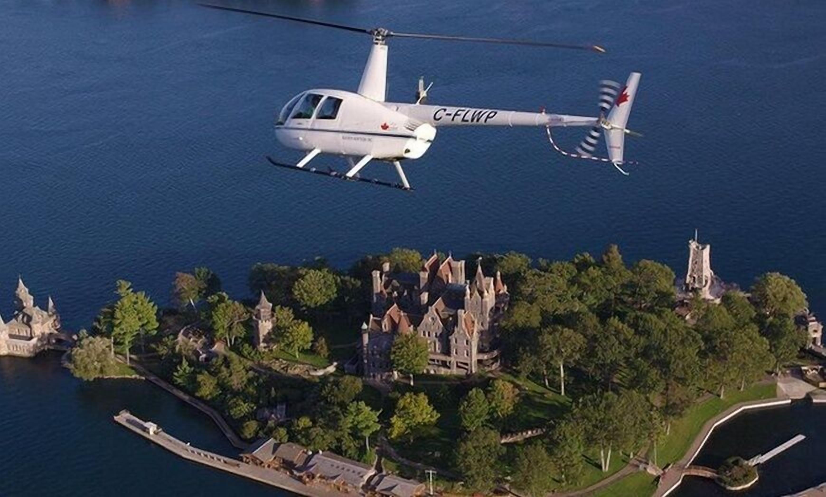 A helicopter with the registration C-FLWP flying over a coastal area with historic buildings and a dock.