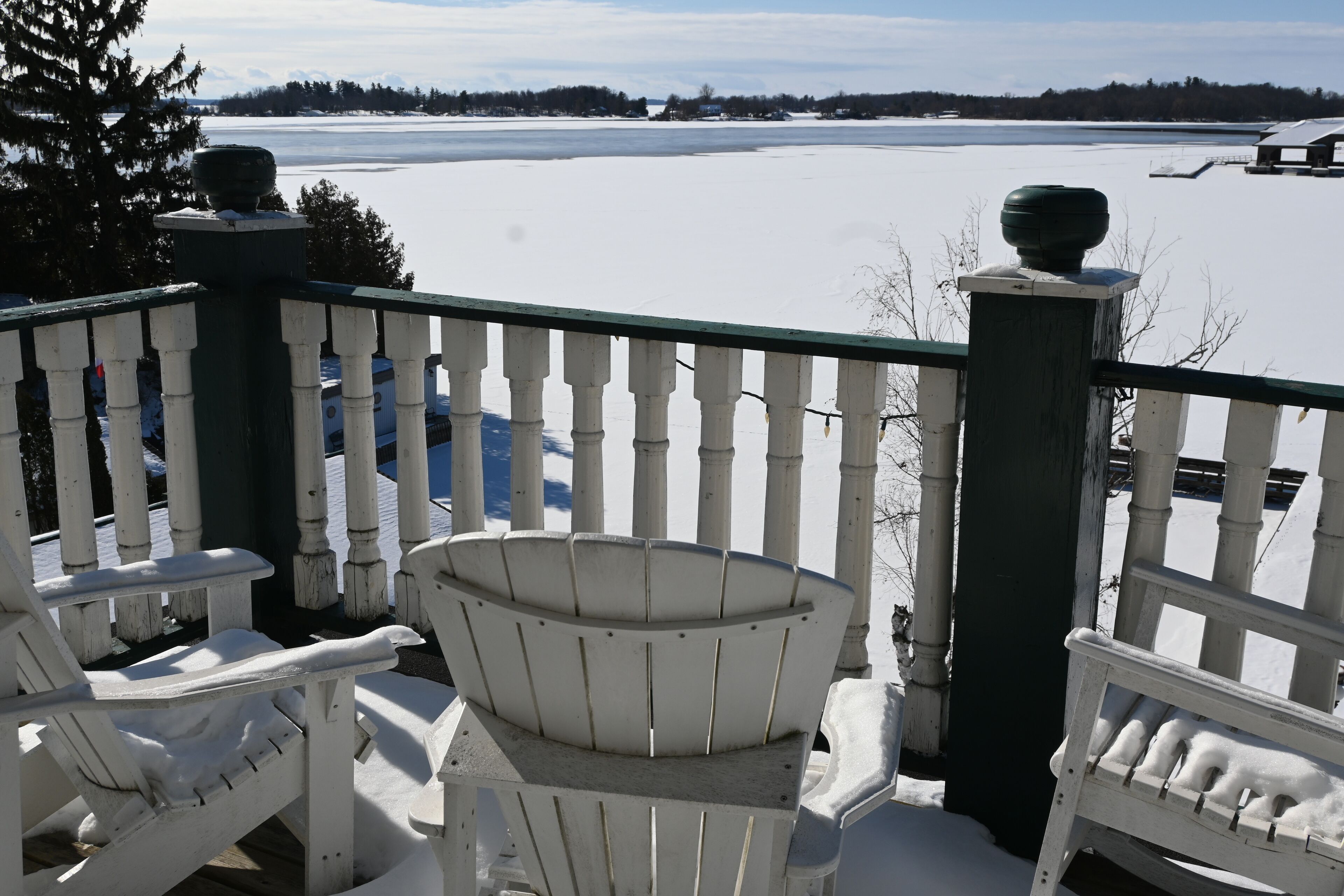 A balcony with white Adirondack chairs and a view of a frozen lake.