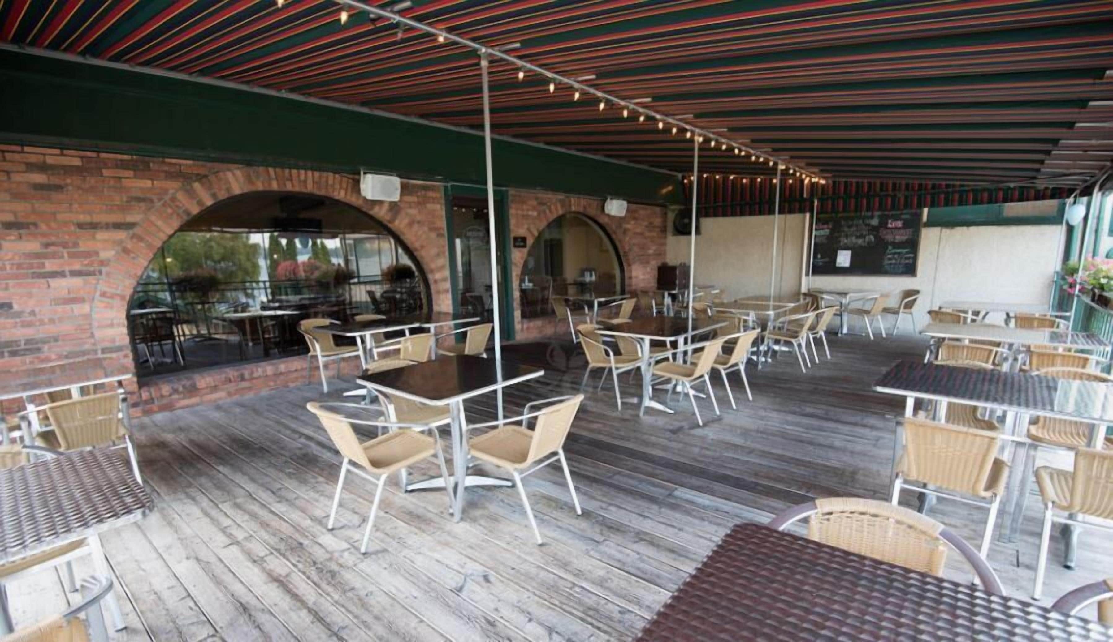An outdoor patio area with brick arches, wooden flooring, and tables and chairs.
