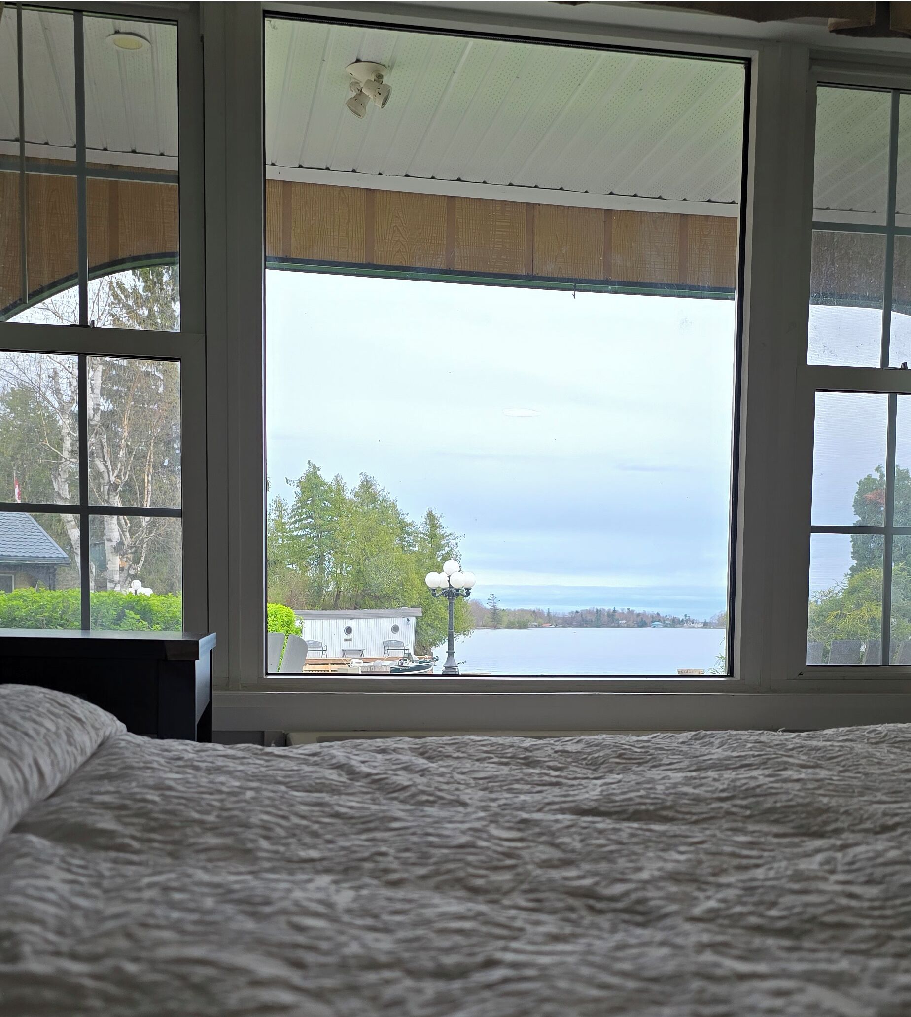 Une chambre avec une grande fenêtre donnant sur un lac, un quai et un petit chalet.