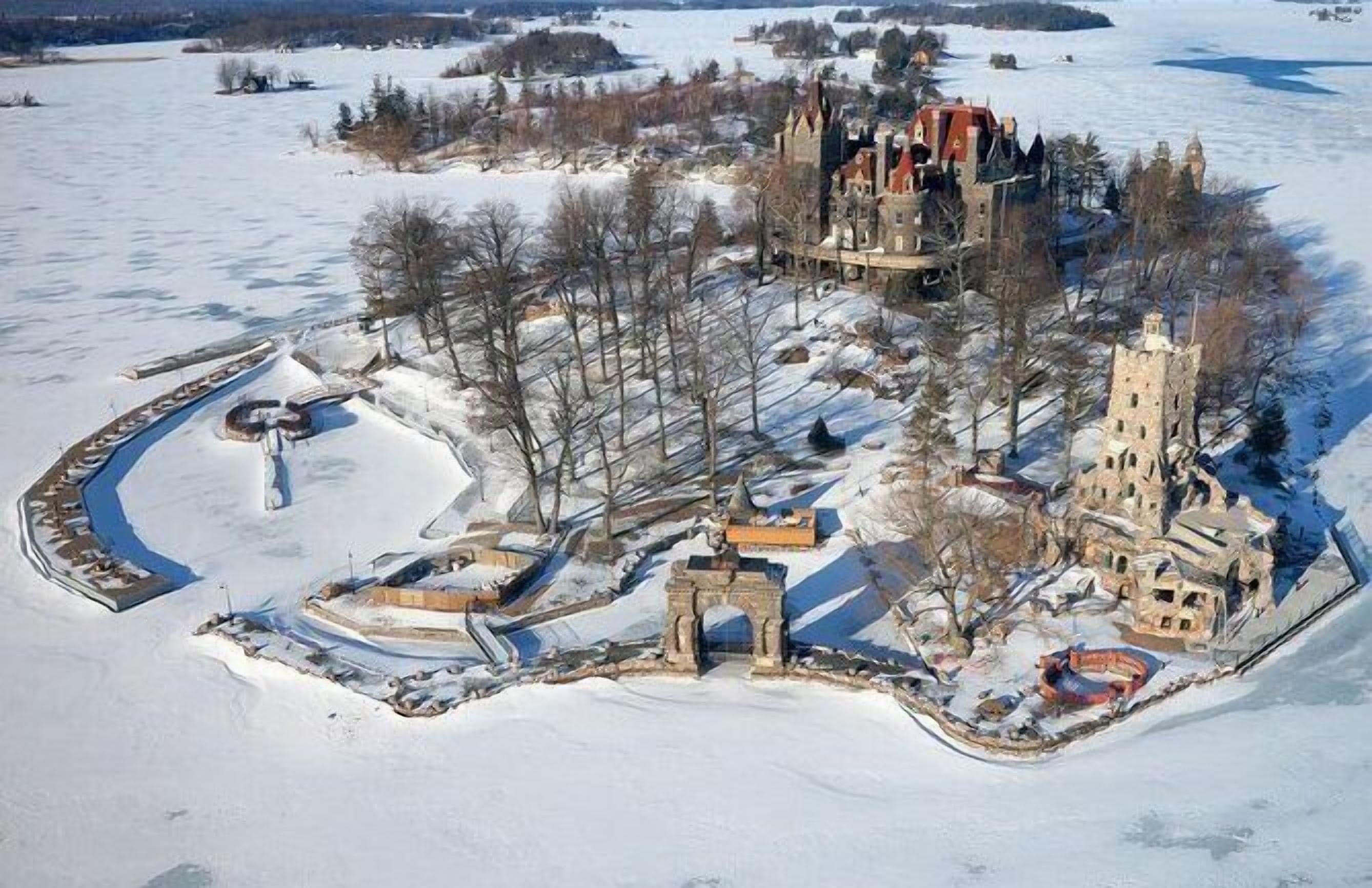 An aerial view of a historic castle surrounded by snow-covered land, with a moat and a bridge leading to the entrance.