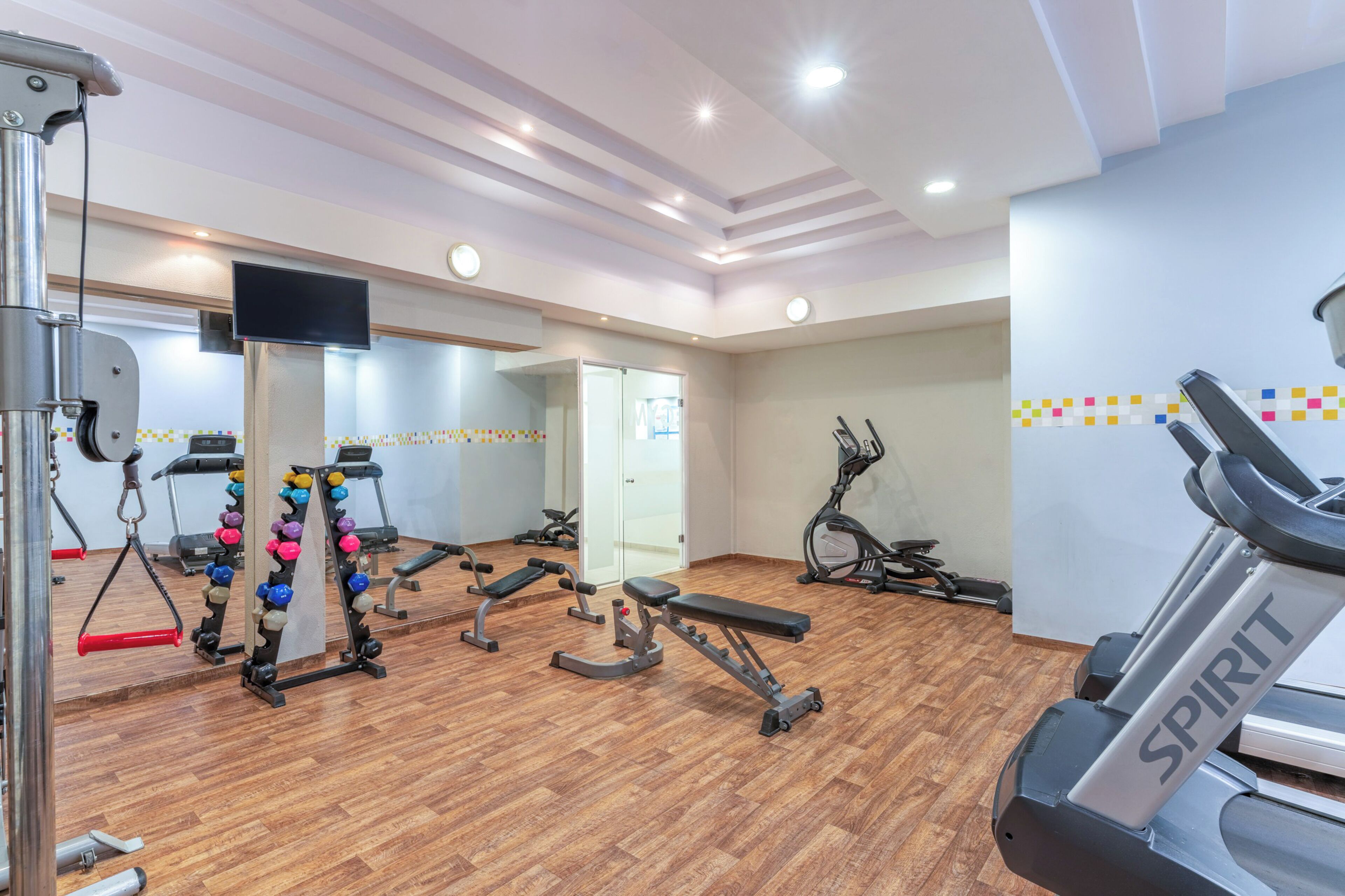 Un gimnasio con equipo de ejercicio diverso, una cinta de correr y un espejo grande.