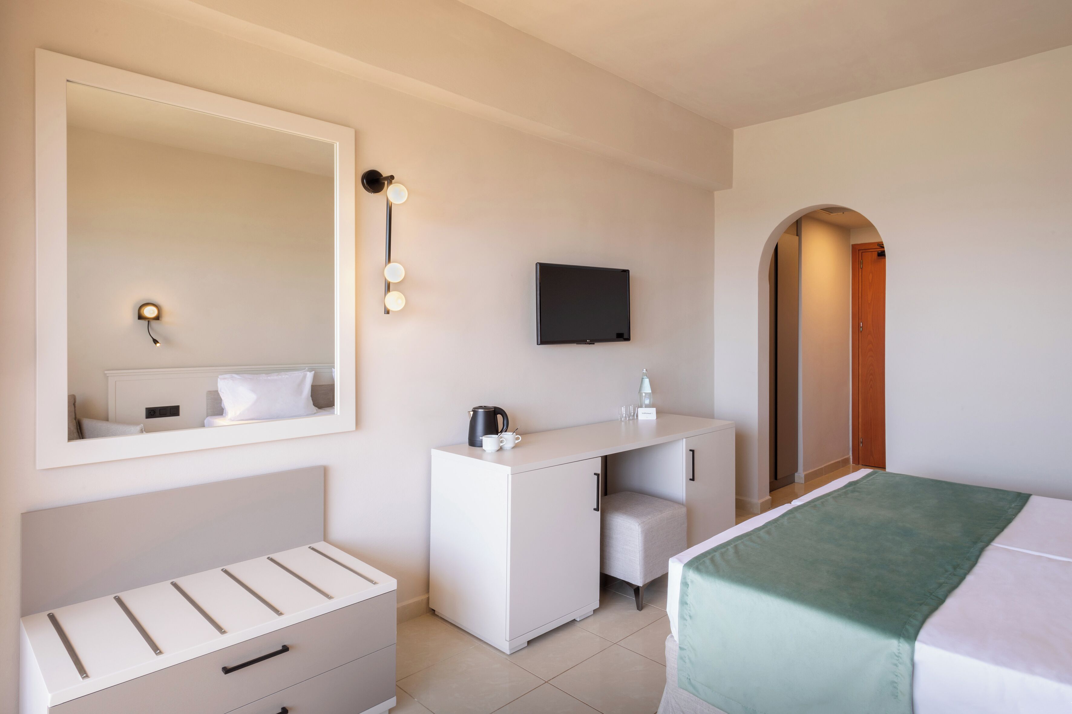 A hotel room with a bed, a desk, a mirror, a television, and a wardrobe.