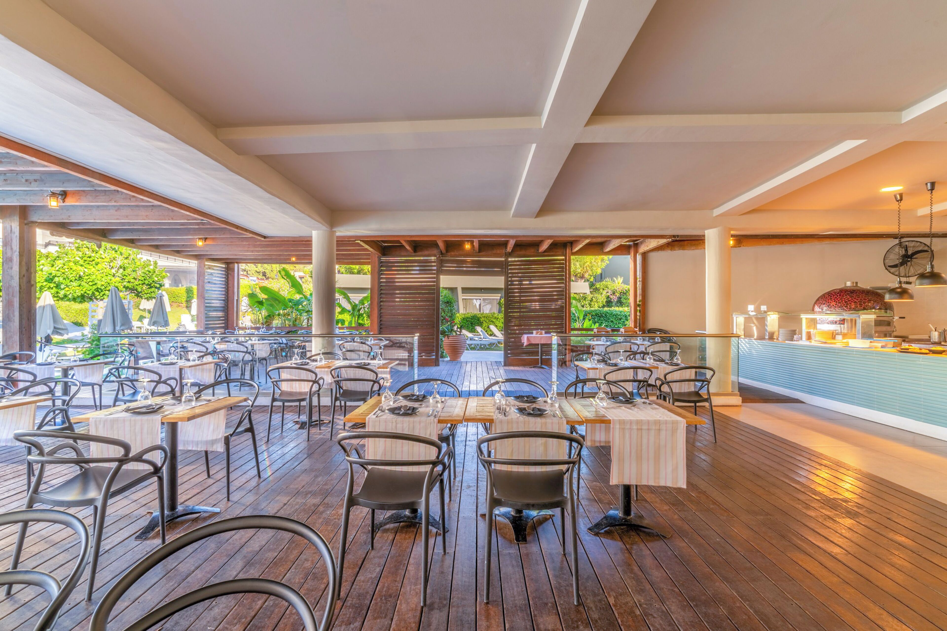 An outdoor dining area with multiple tables and chairs, a wooden deck, and a view of greenery.