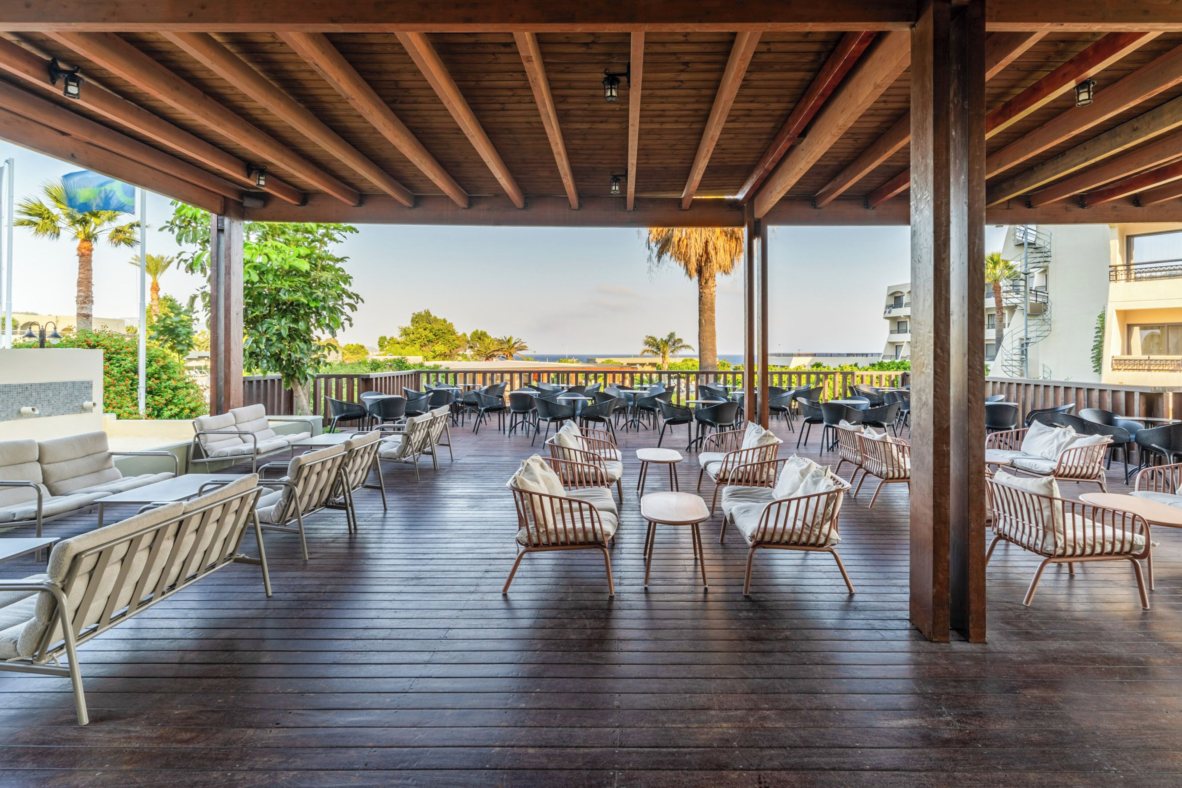 Un patio exterior con suelo de madera, mobiliario de metal y mimbre, y vista al océano.