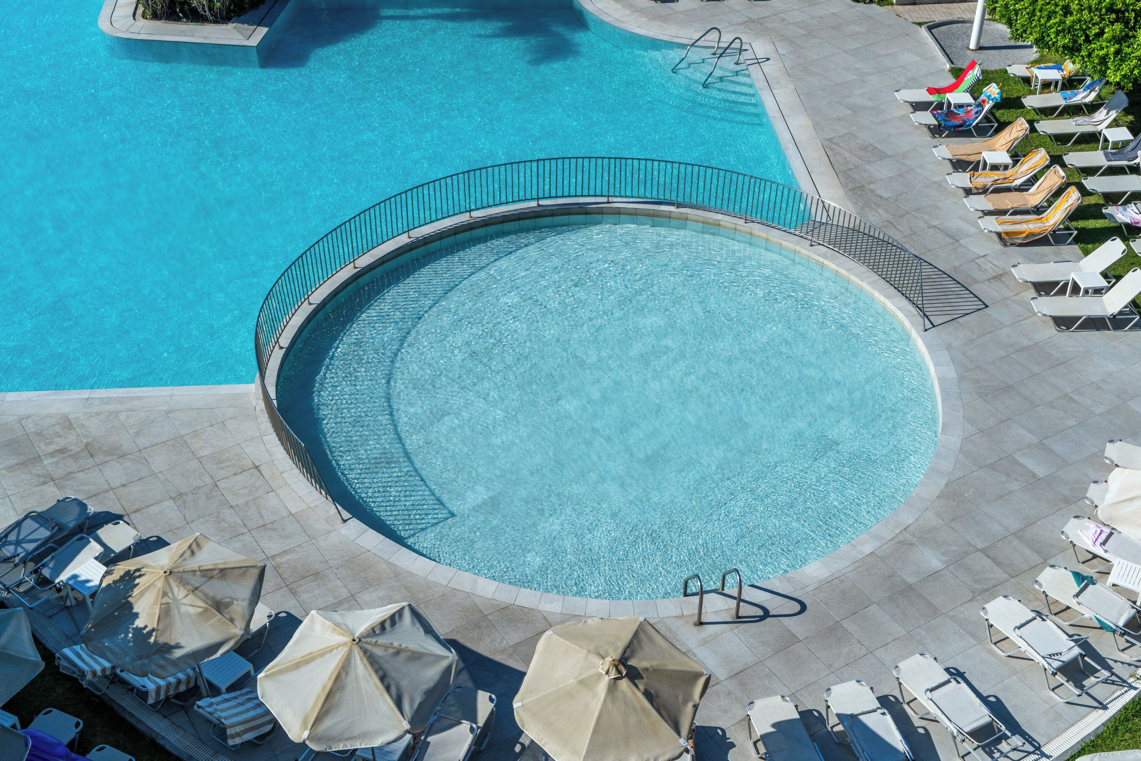 Ein runder Pool mit einer umlaufenden Promenade, Liegestühlen und Sonnenschirmen.