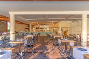 A restaurant with multiple tables and chairs, a kitchen area in the background, and a view of the outdoors. - Sol Cosmopolitan Rhodes - All inclusive (Rhodes)