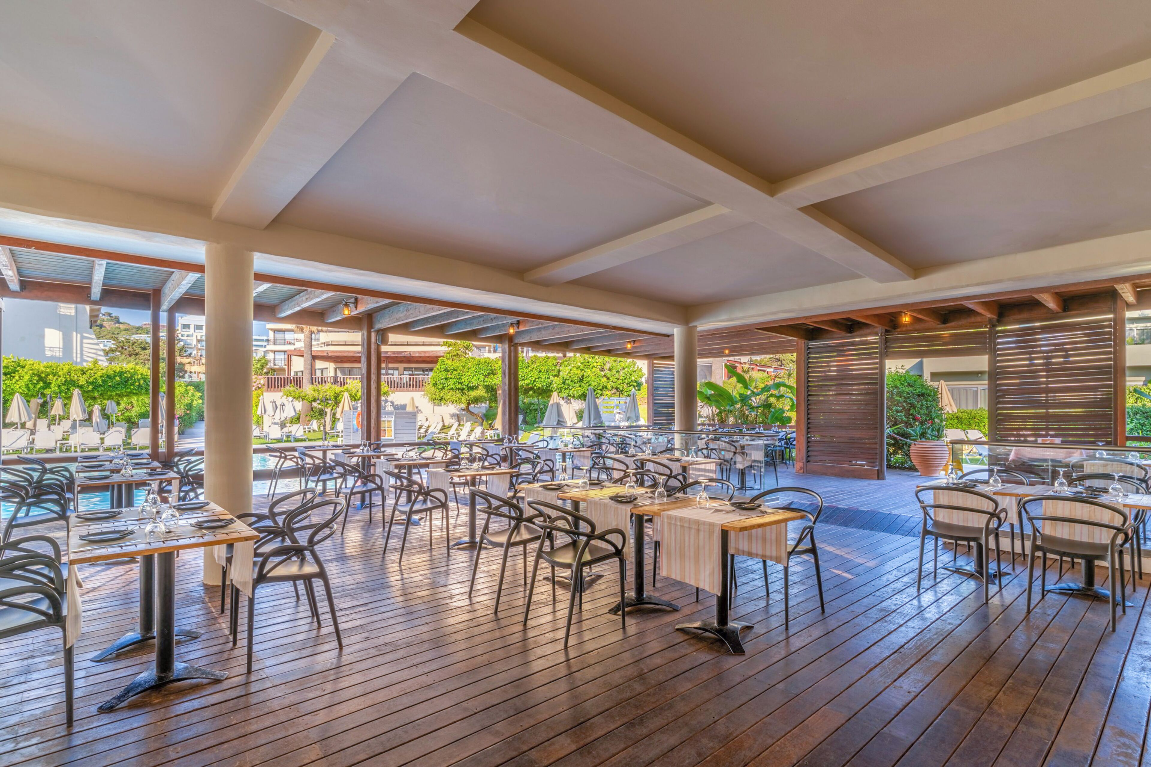 An outdoor dining area with multiple tables and chairs, a wooden deck, and a view of the surrounding landscape.