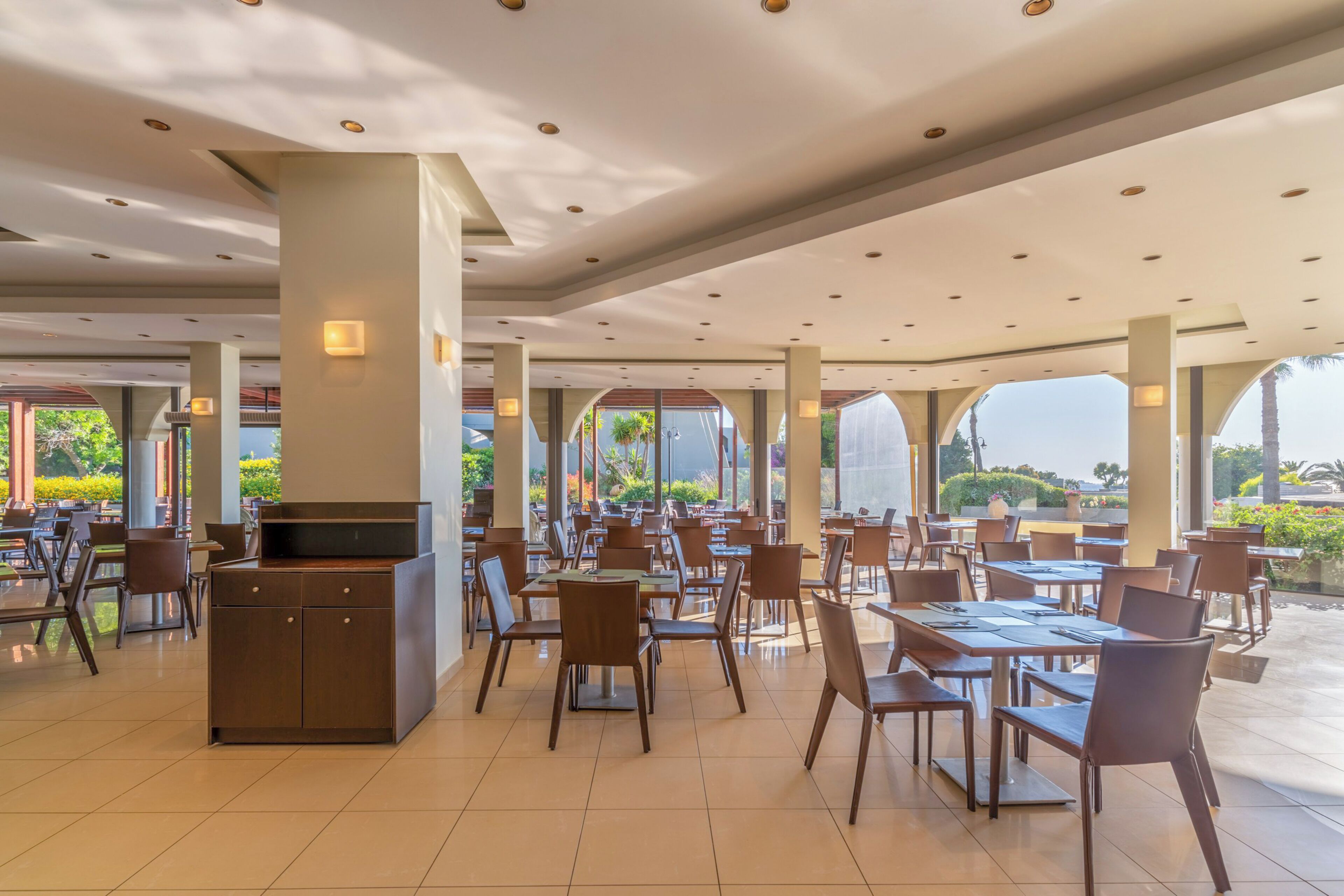 A spacious indoor dining area with multiple tables and chairs, large windows, and a central pillar.