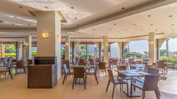 A spacious indoor dining area with multiple tables and chairs, large windows, and a central pillar.