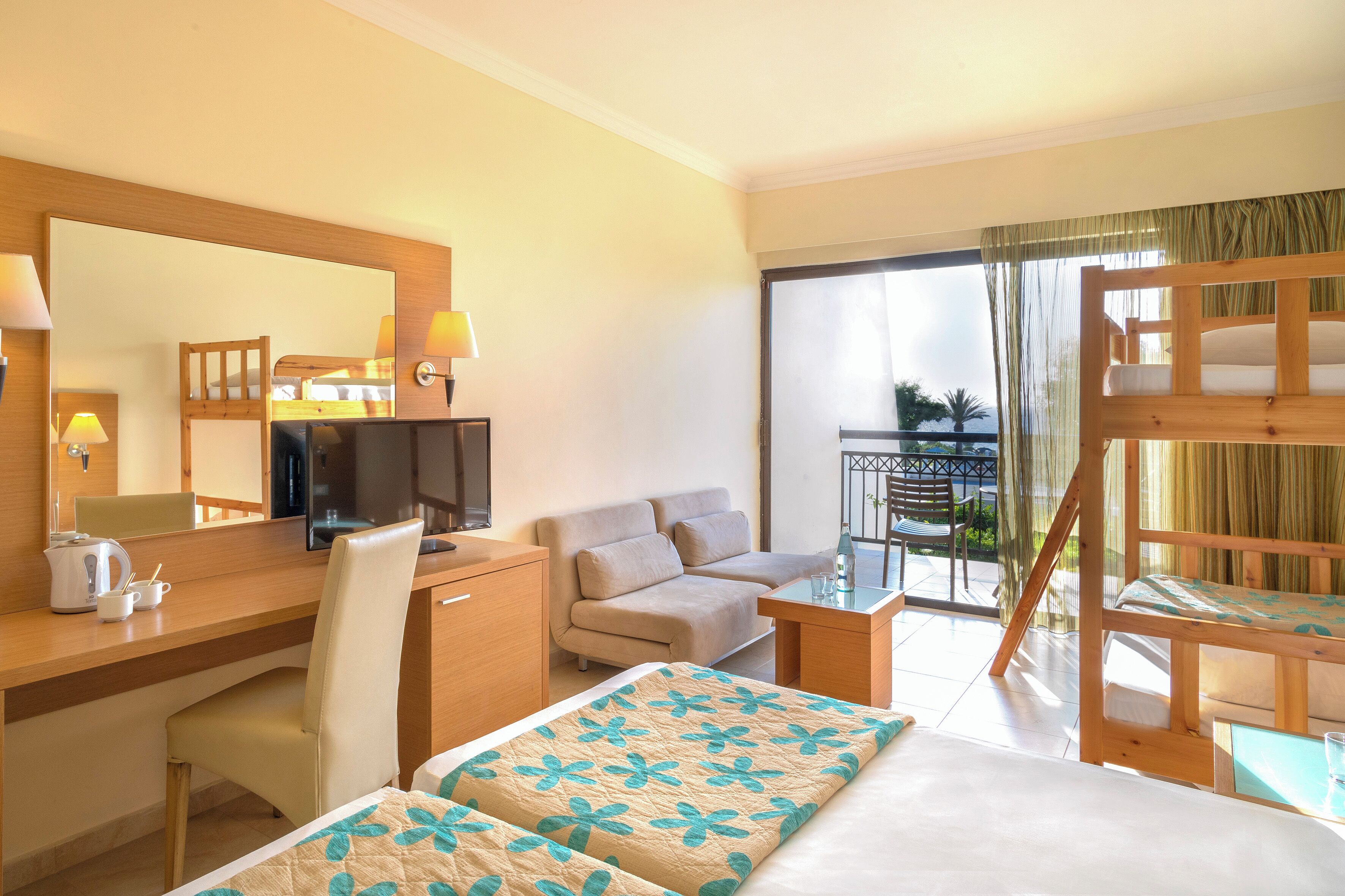 A hotel room with a bed, desk, chair, sofa, and a balcony with a view.