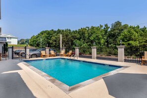 A rectangular swimming pool with a tiled edge, surrounded by a black metal fence, and wooden lounge chairs along the poolside. - Sleep Inn & Suites Millbrook - Prattville (Millbrook)