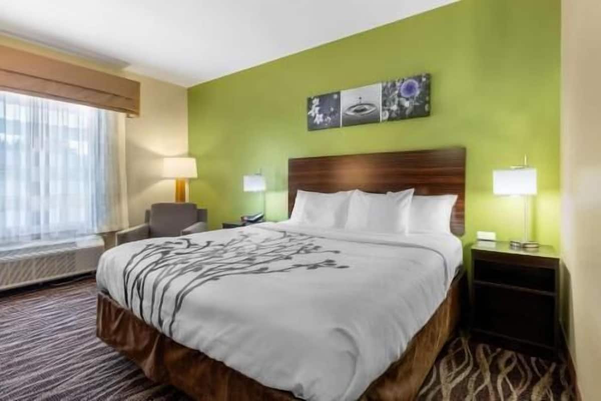A hotel room with a large bed, two bedside tables with lamps, a chair, and a window with curtains.