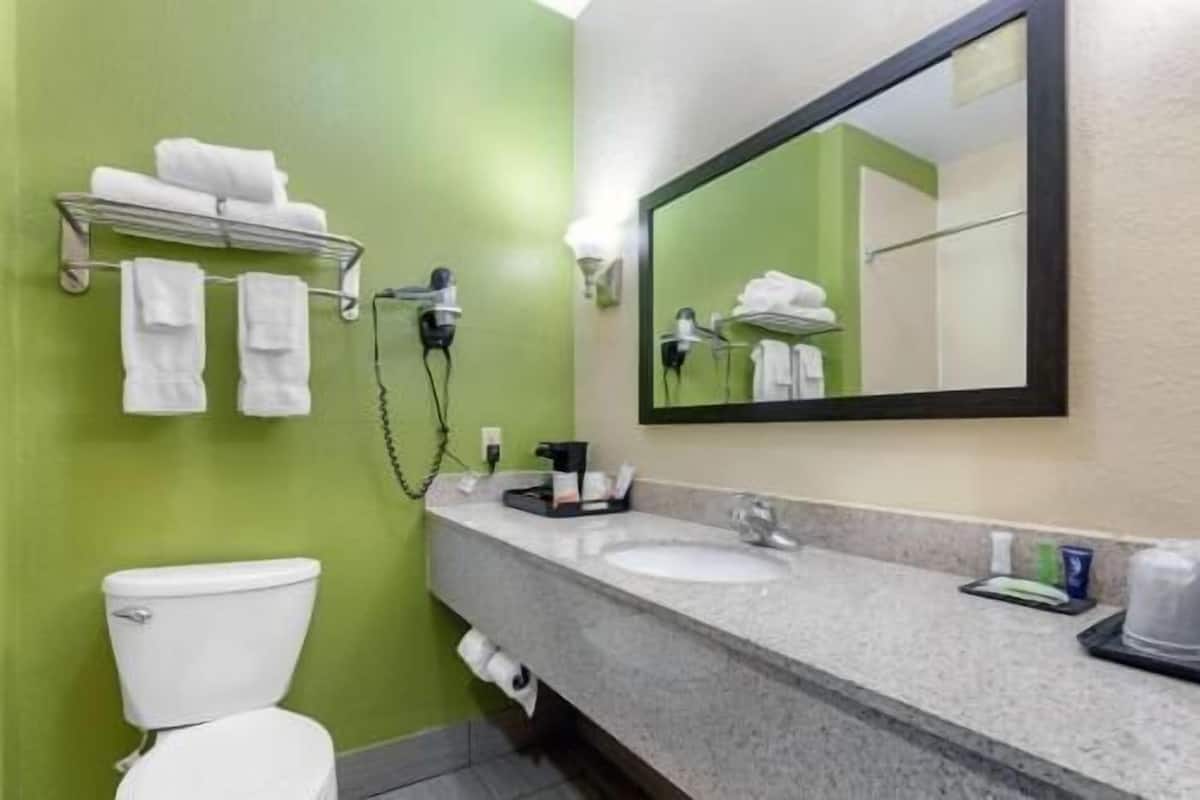 A bathroom with a green wall, a white toilet, a sink with a mirror above it, and a towel rack with towels.