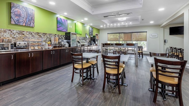 A modern kitchen with dark wooden cabinets, a stone backsplash, and a dining area with wooden chairs and tables. - Sleep Inn & Suites Millbrook - Prattville (Millbrook)