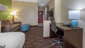 A hotel room with a bed, a desk, a chair, a blue ottoman, a lamp, and a wall-mounted TV. - Sleep Inn & Suites Millbrook - Prattville (Millbrook)