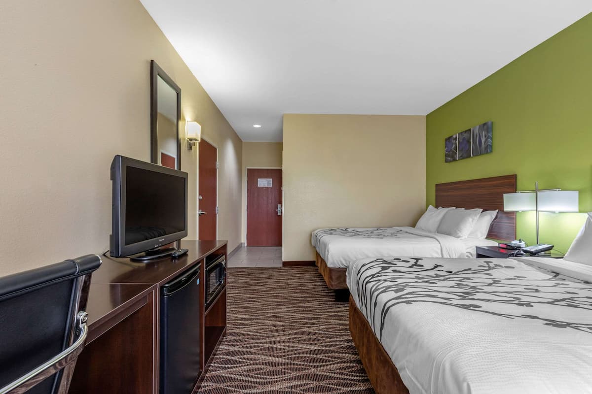 A hotel room with two beds, a TV, a desk, and a mirror.