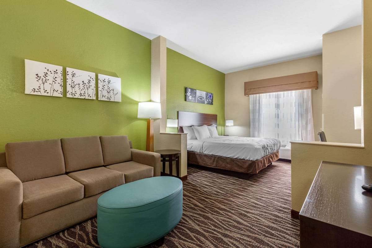 A hotel room with a sofa, a bed, a small table, and artwork on the walls.
