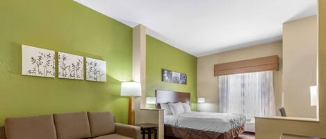 A hotel room with a sofa, a bed, a small table, and artwork on the walls.