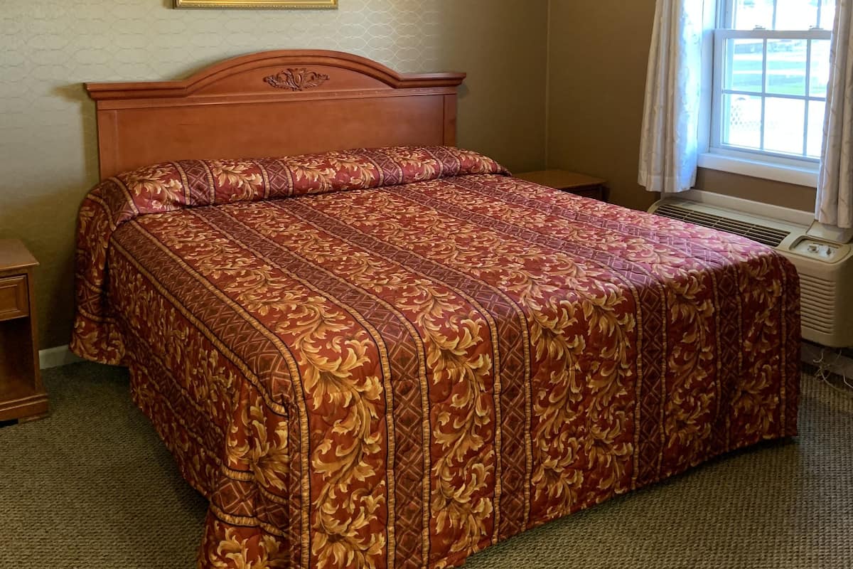 A hotel room with a wooden bed, a framed floral artwork on the wall, and a window with curtains.