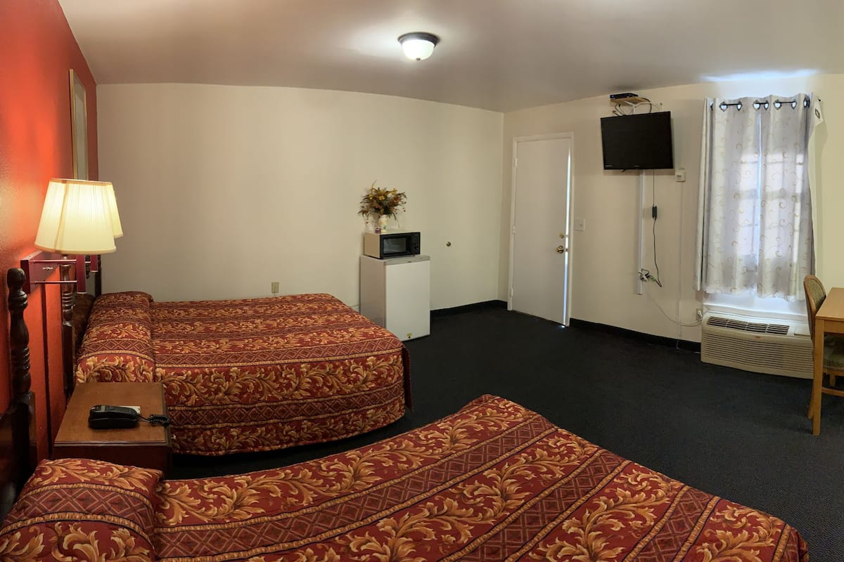 A hotel room with a sofa bed, a desk with a chair, a TV mounted on the wall, and a window with a curtain.