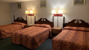 A hotel room with four single beds, each with a wooden headboard and a patterned bedspread. There are two bedside tables with lamps, and the walls are adorned with framed artwork. - Dutch Motel Palmyra (Palmyra)