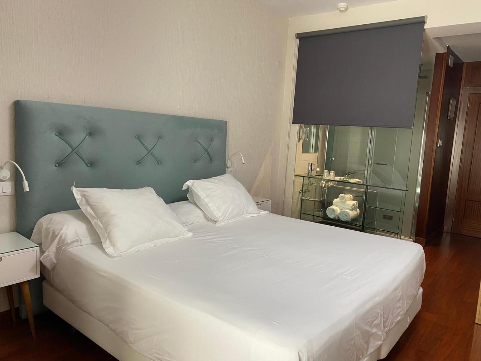 A neatly made bed with white linens and a teal headboard with a unique X-shaped design.