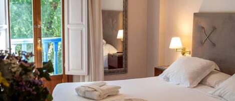 A hotel room with a bed, two bedside lamps, a mirror, and a window with a view of greenery.