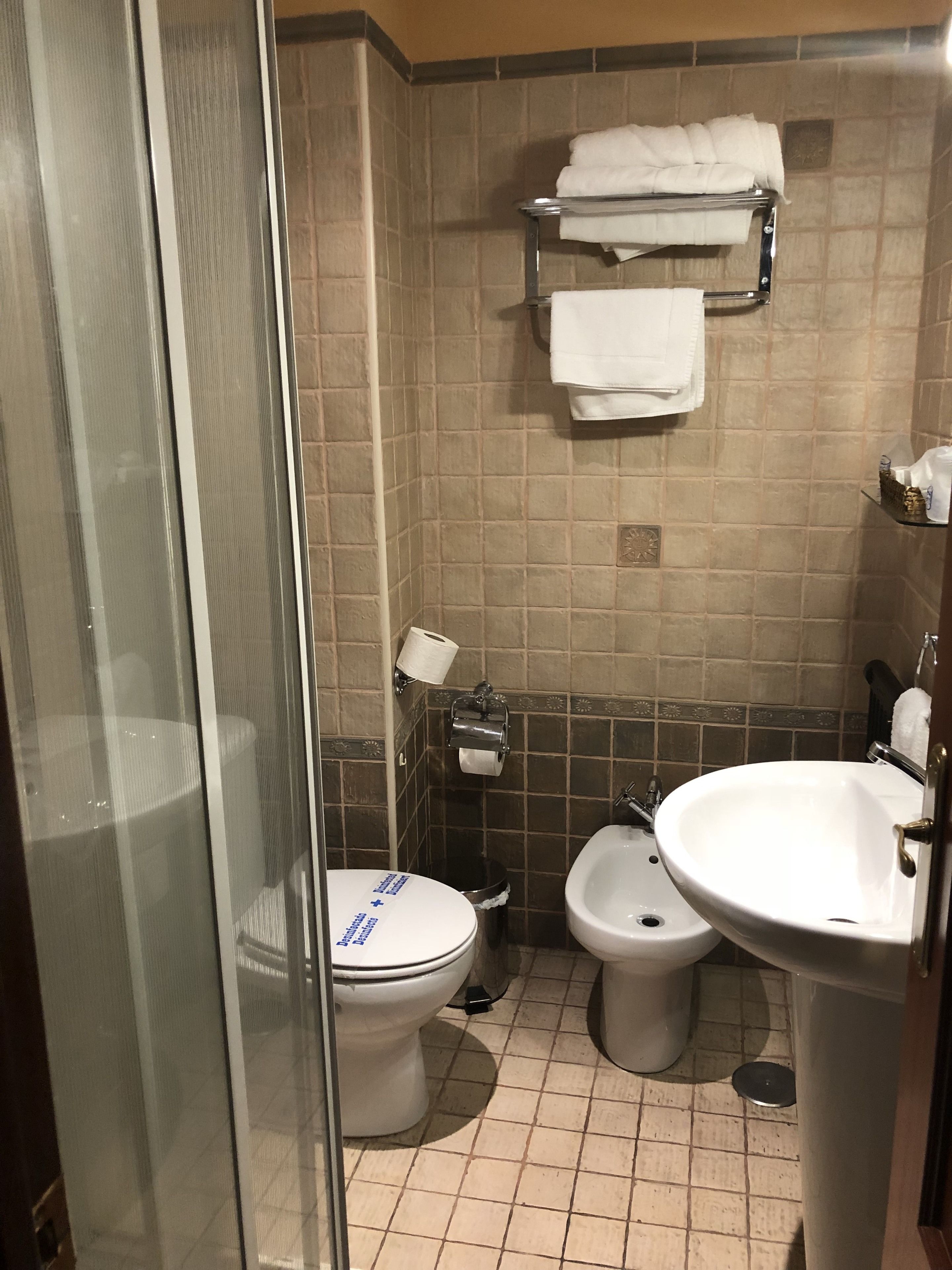 A bathroom with a toilet, bidet, and sink, tiled walls, and a towel rack.