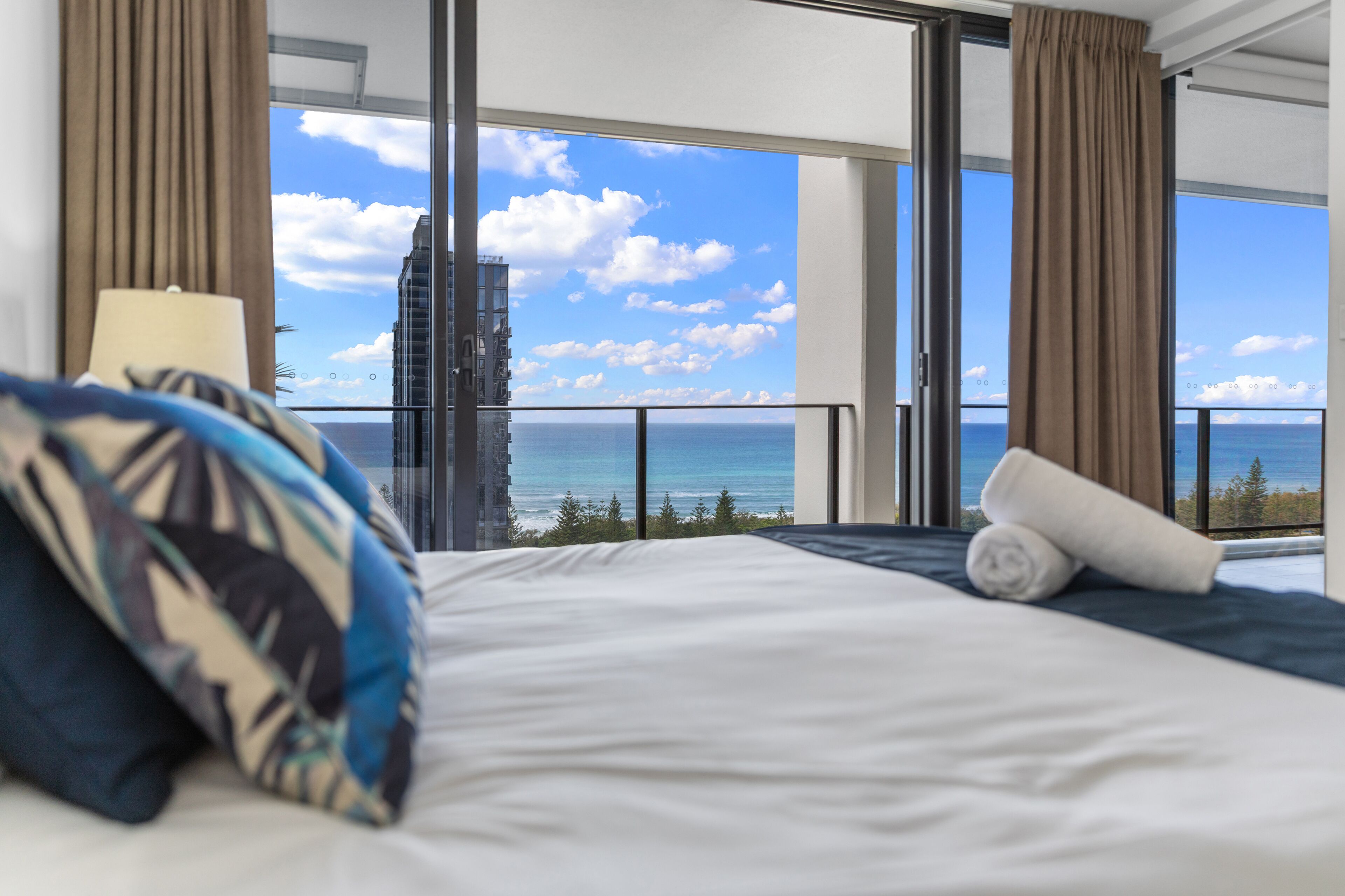 A hotel room with a bed, a view of the ocean, and a building in the distance.