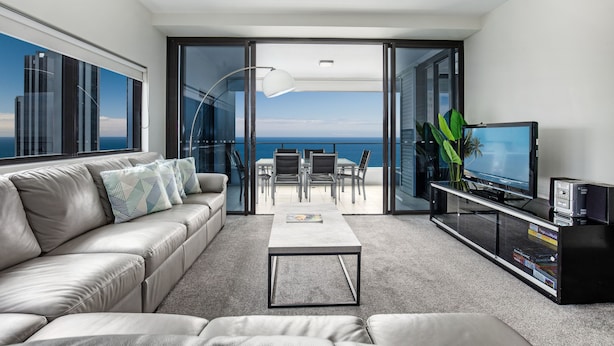 Una sala de estar moderna con sofá, mesa de centro y televisor, con un balcón y vista al océano.