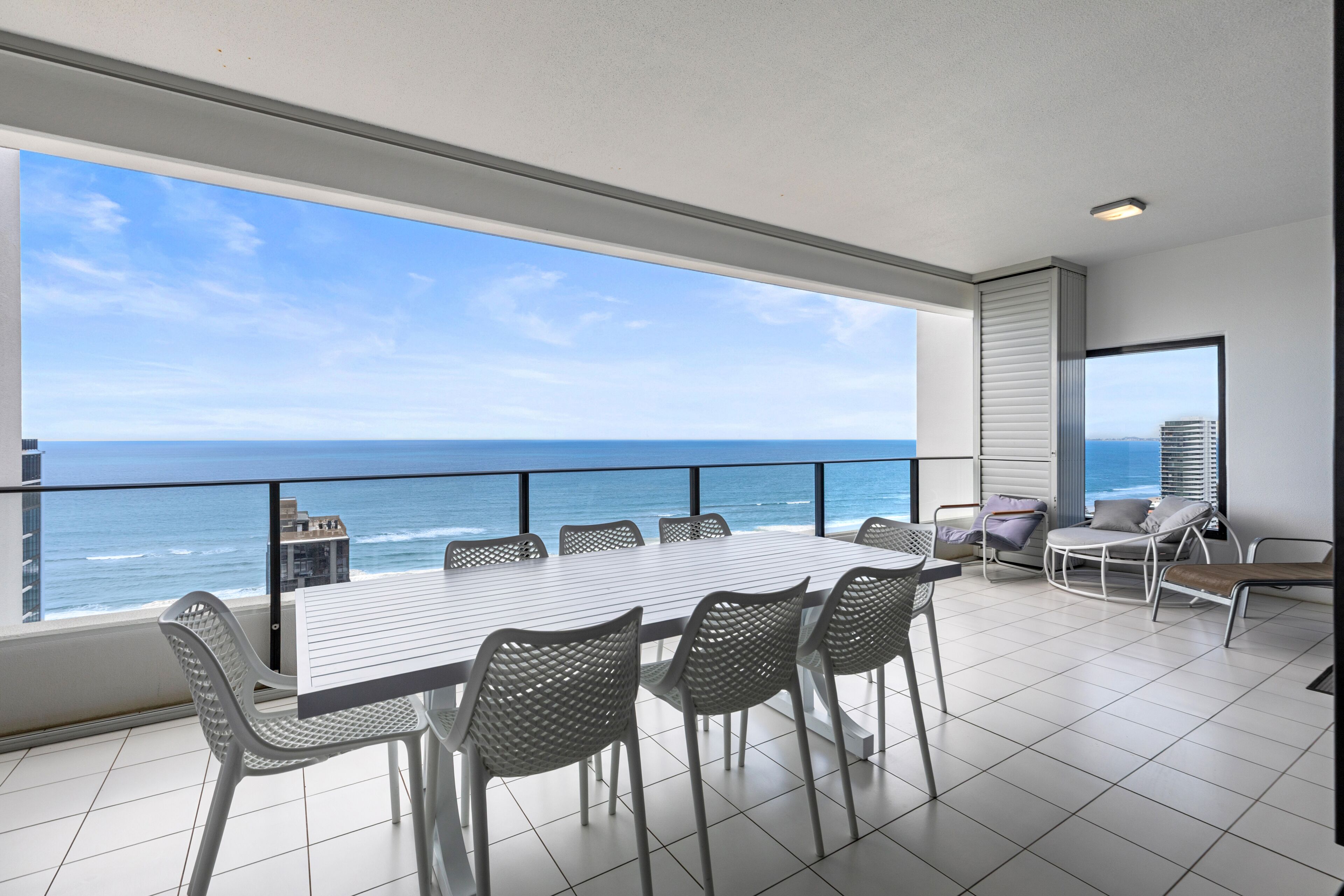 A balcony with a view of the ocean, a table with chairs, and a seating area with a chair and a sofa.