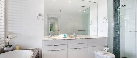 A modern bathroom with a large mirror, a bathtub, a toilet, and a glass-enclosed shower area.