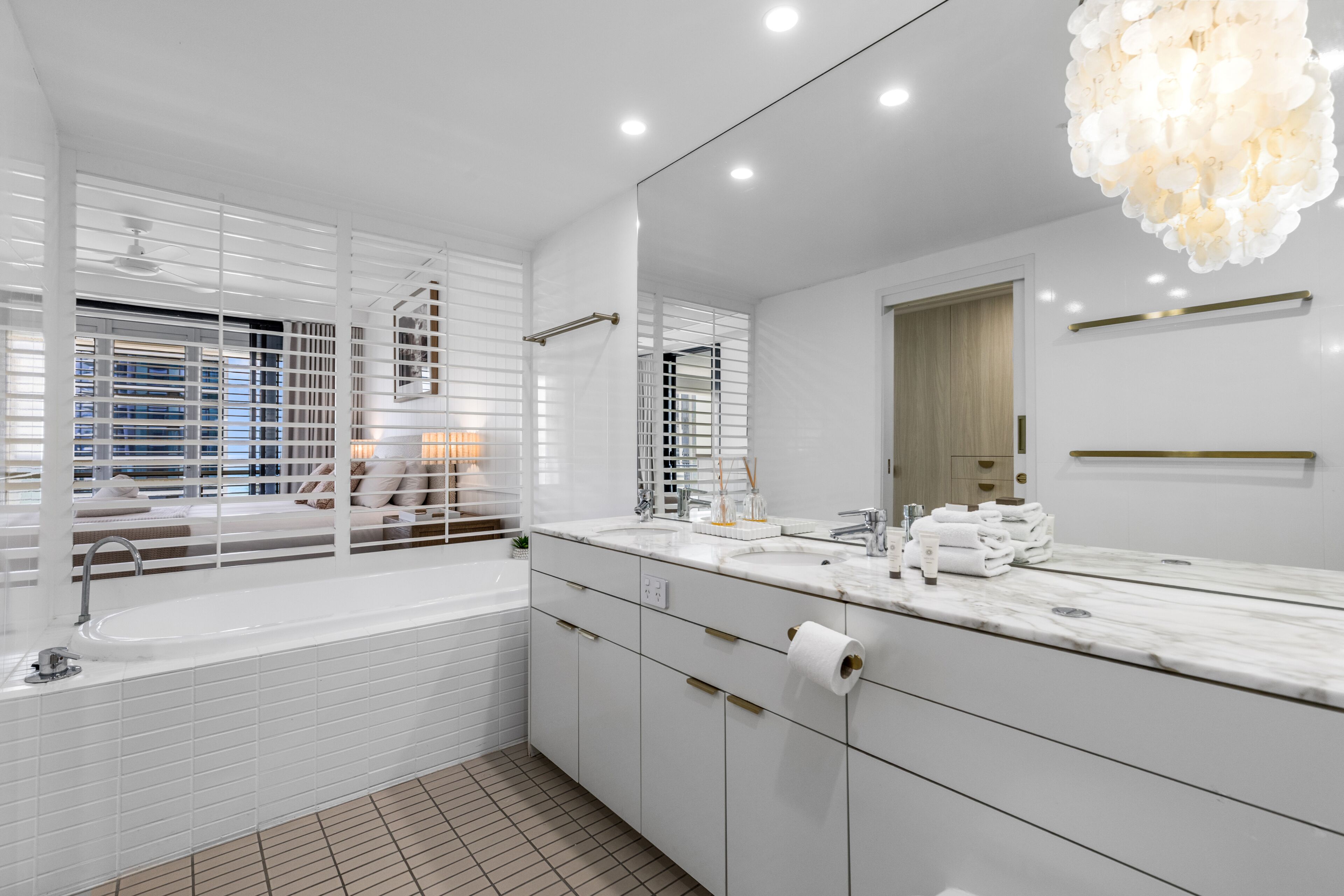 A modern bathroom with a large mirror, white tiles, a bathtub, and a vanity with a marble countertop.