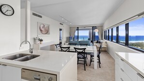 Una cocina moderna con lavavajillas integrado, un comedor con mesa y sillas, y un amplio ventanal con vistas al océano.