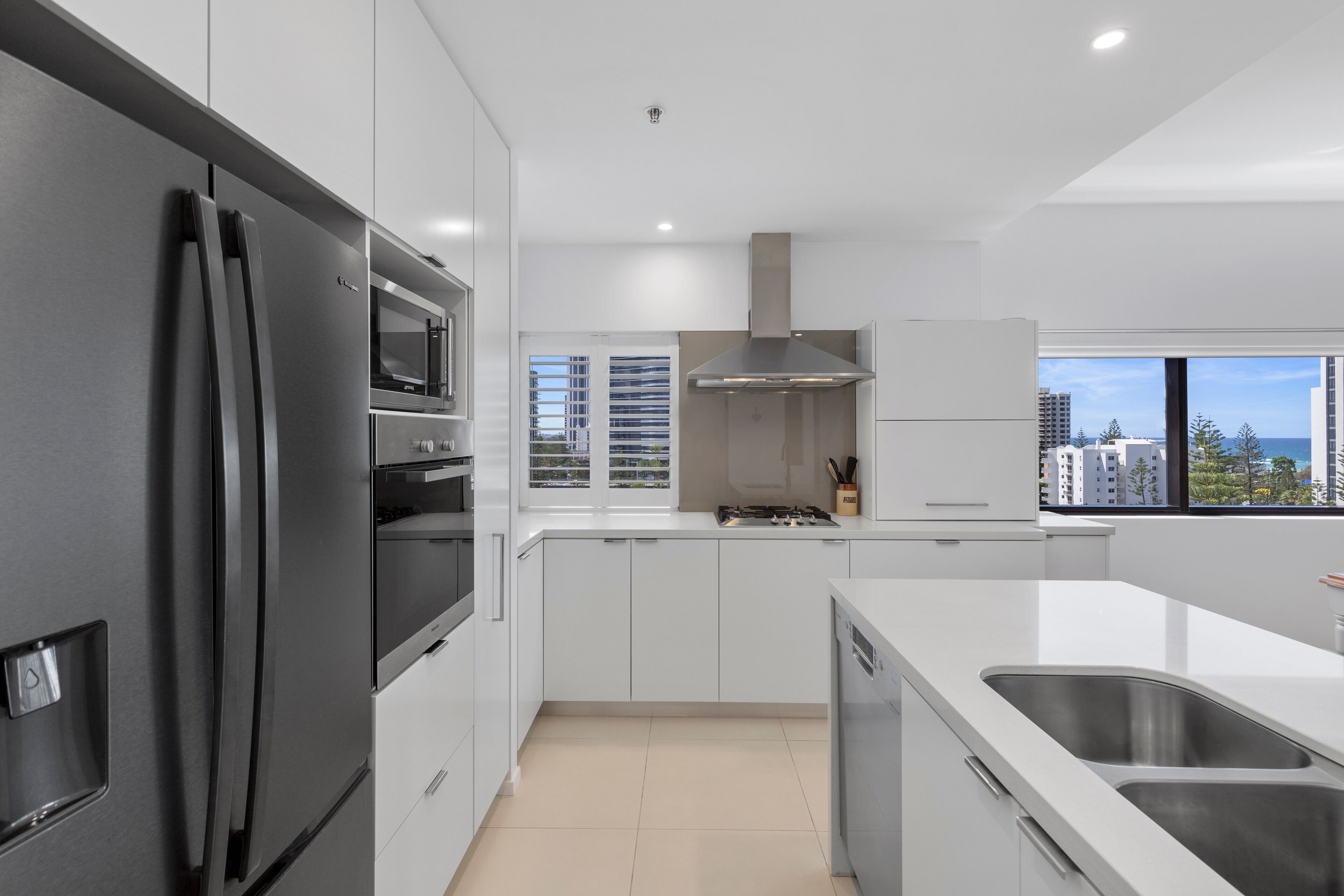 Una cocina moderna con armarios blancos, electrodomésticos de acero inoxidable y vistas de la ciudad a través de amplios ventanales.