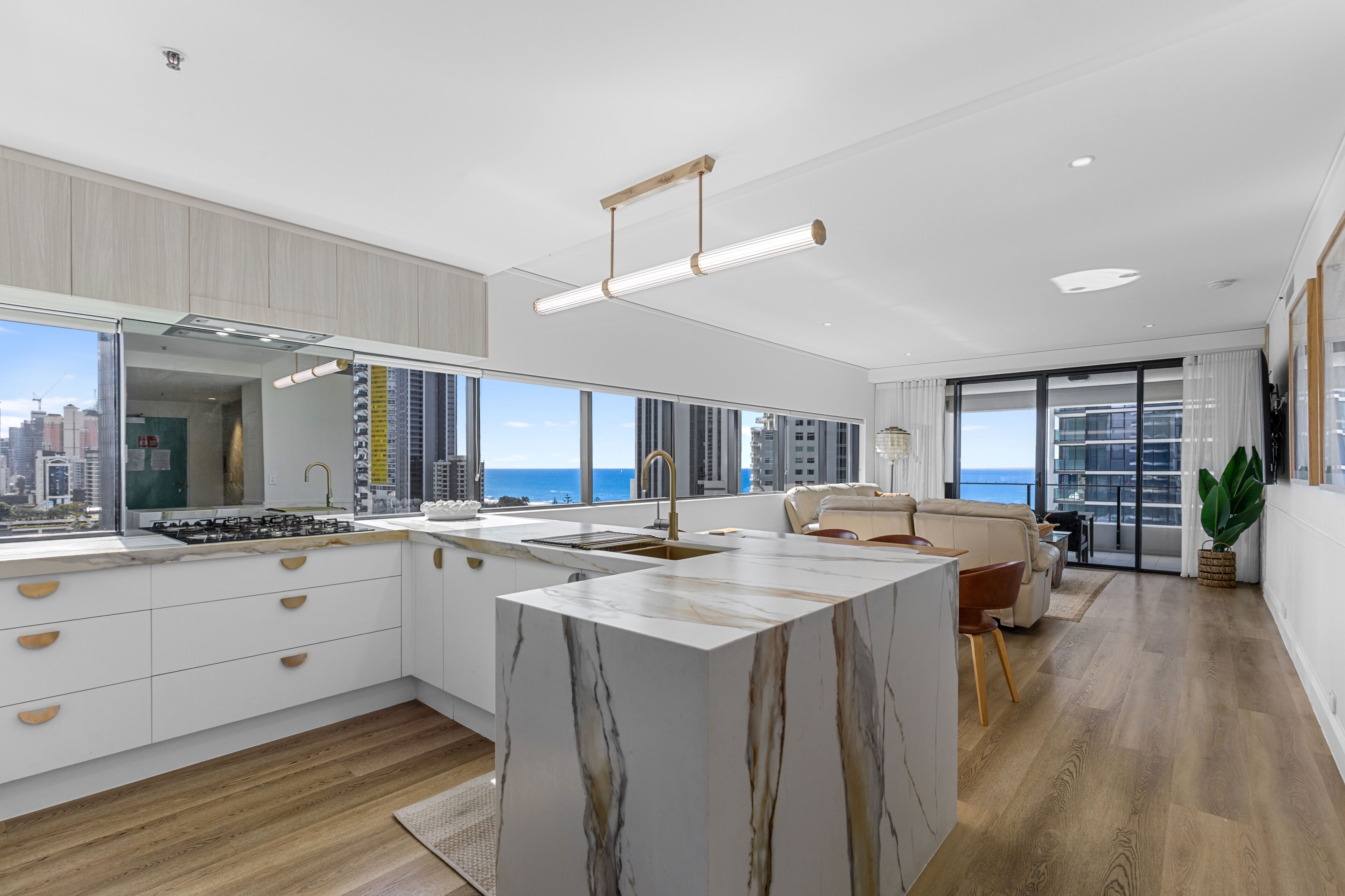 A modern kitchen with a large island, a dining area with a sofa, and a view of the city and ocean.