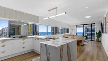 Eine moderne Küche mit einer großen Kochinsel, einem Essbereich mit einer Couch und Blick auf Stadt und Meer.