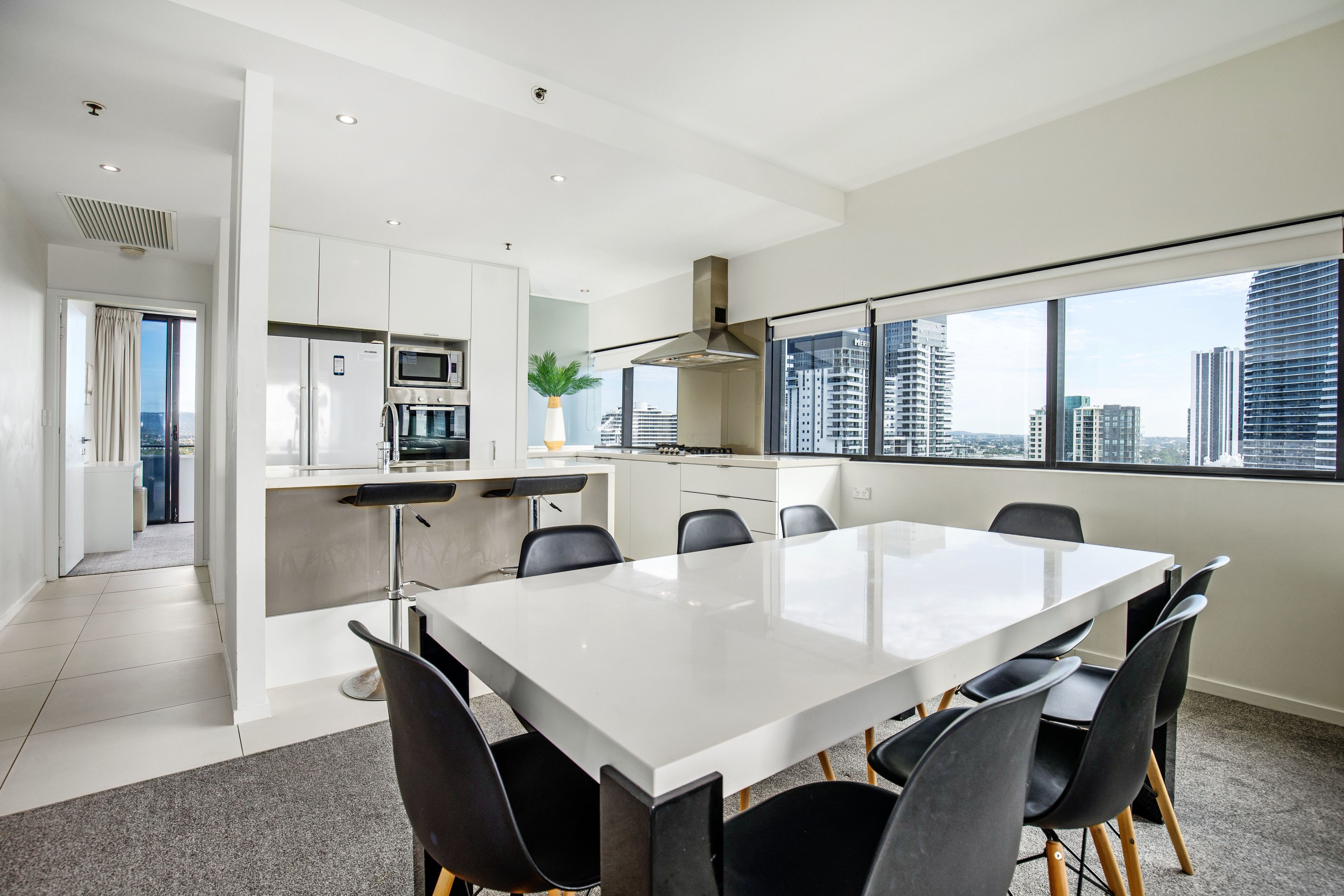 A modern kitchen with white cabinetry, a stainless steel refrigerator, and a microwave. There is a dining area with a white table and black chairs.