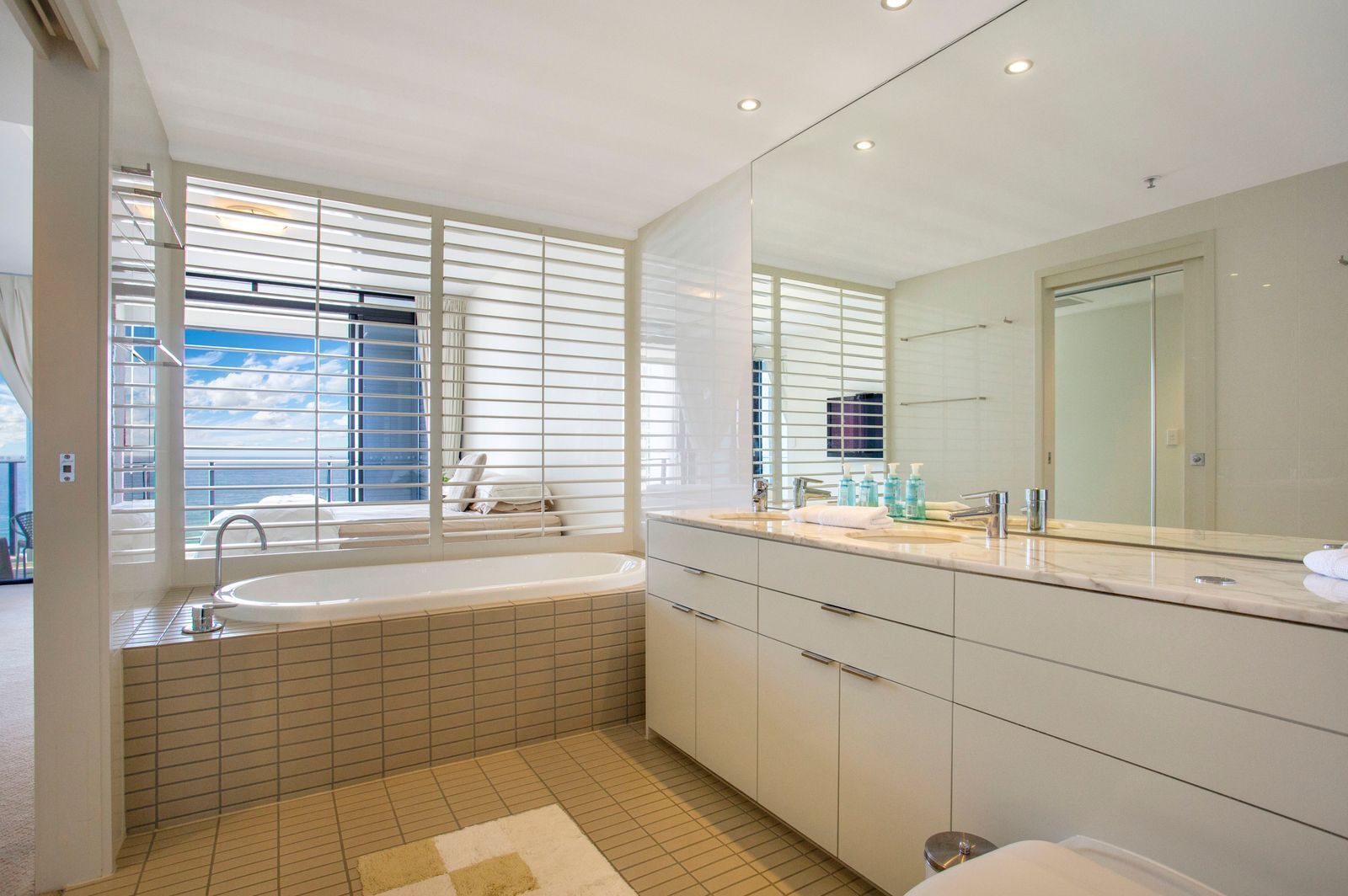 A modern bathroom with a bathtub, a large mirror, and a window with blinds.