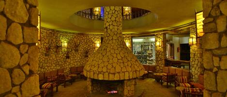 Un vestíbulo con suelo de piedra, chimenea central, zonas de estar y un bar.