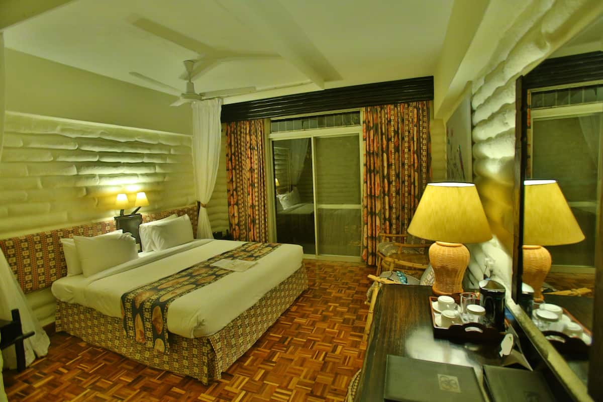 A hotel room with a bed, a desk with a lamp, a chair, a mirror, and a ceiling fan.
