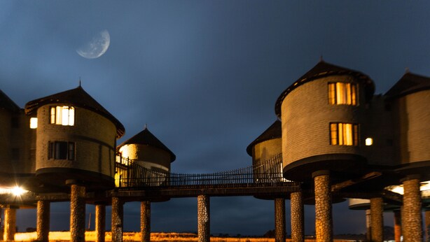 Una serie de torres cilíndricas conectadas por un puente, con un cielo crepuscular y una luna visible.