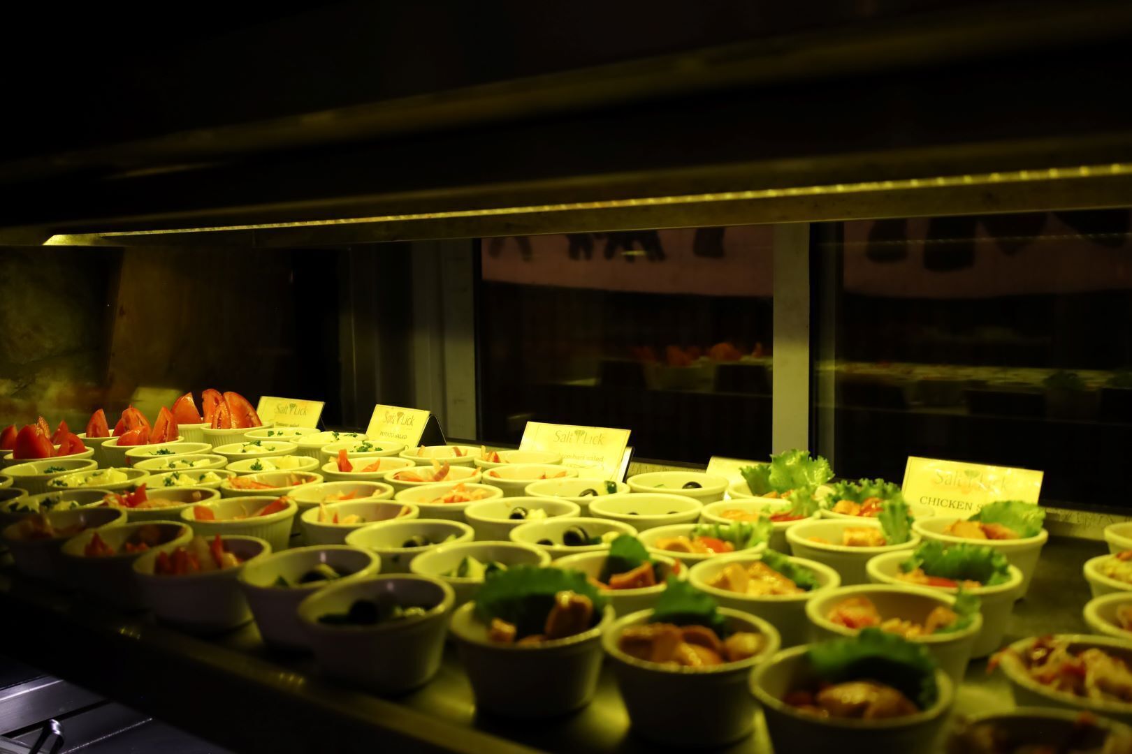 Een buffet met diverse gerechten gepresenteerd in kommen, elk voorzien van een naam.