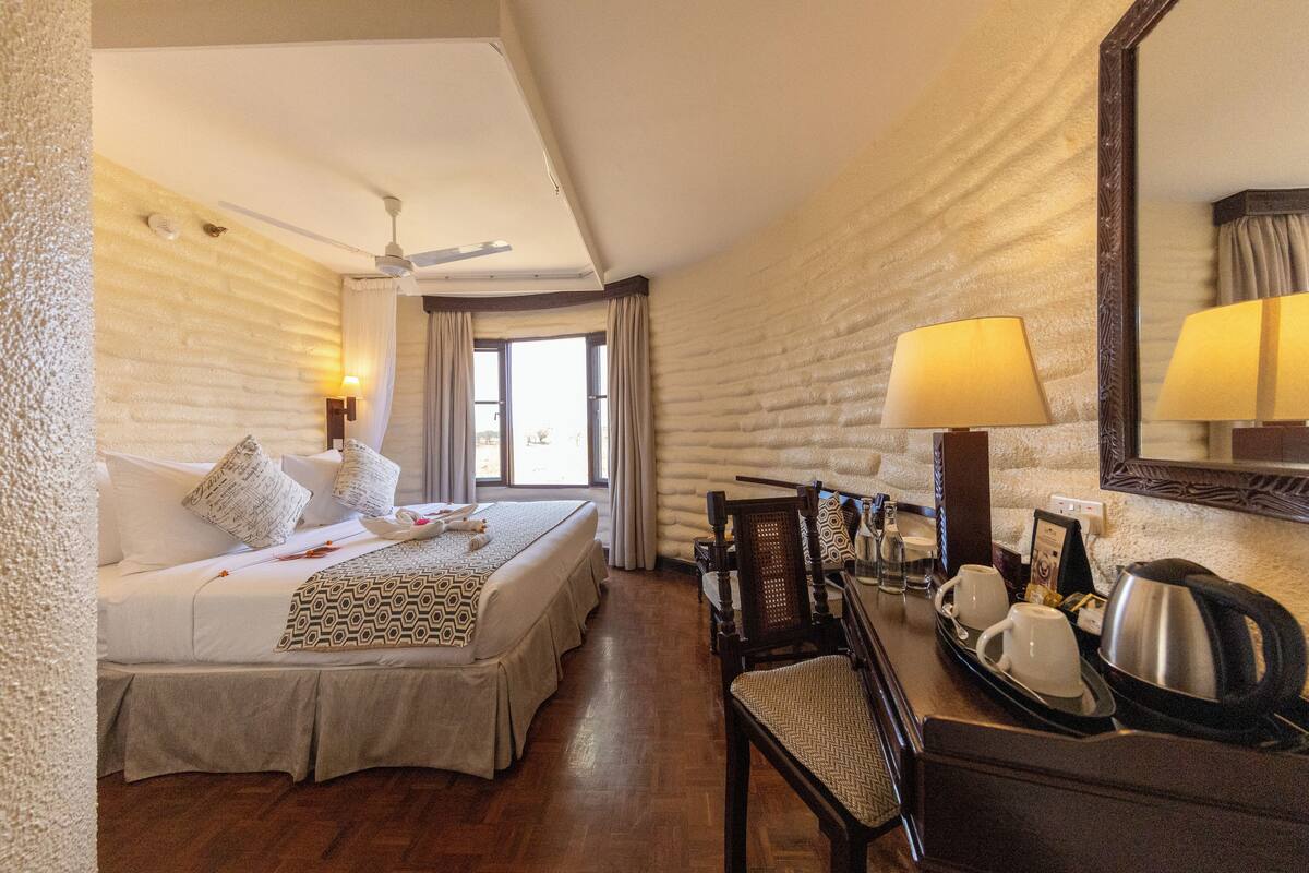 A hotel room with a large bed, a desk with a lamp, and a mirror.