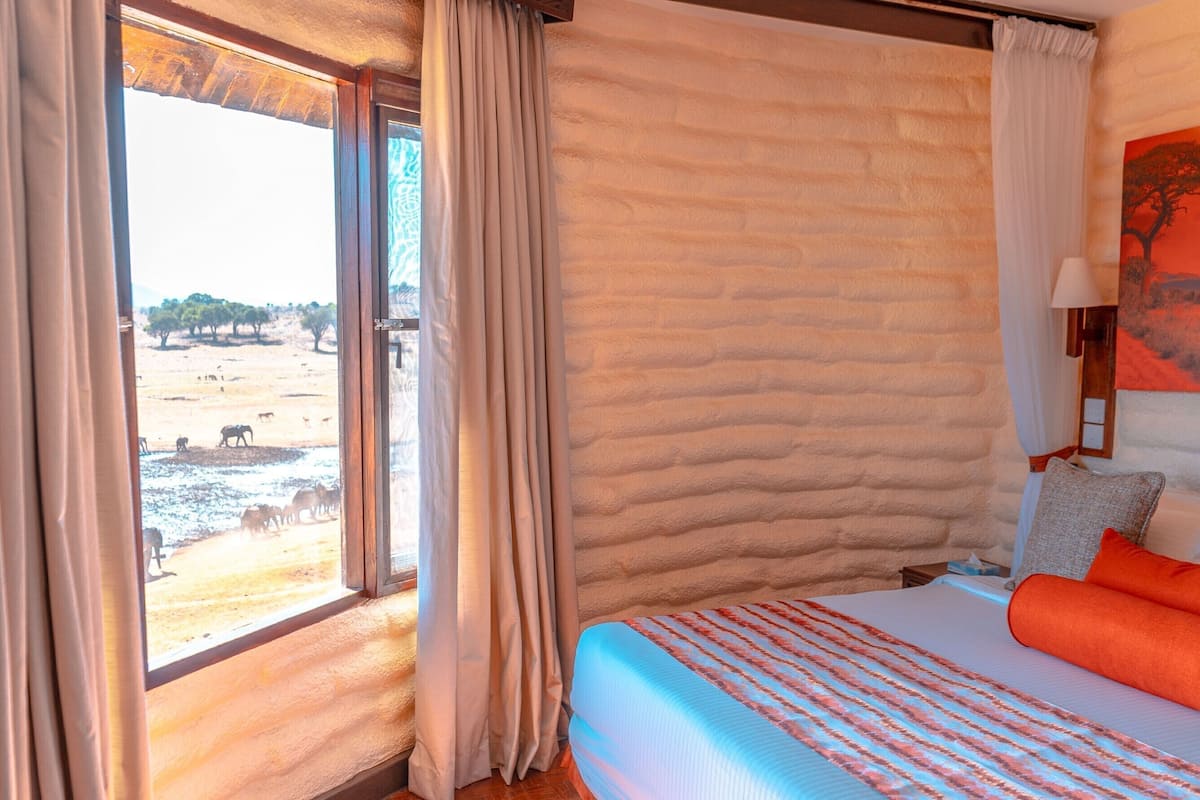 A room with a large bed, a window with curtains, a painting of an elephant, and a view of wildlife outside.