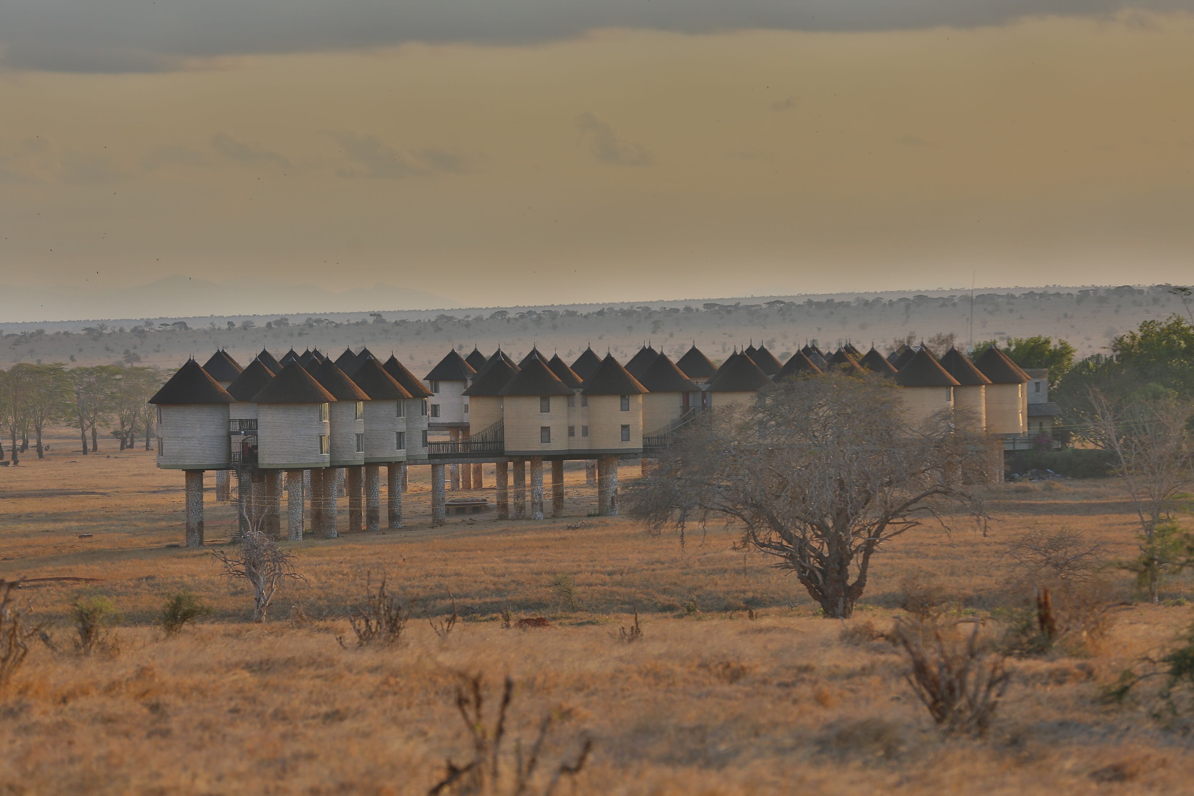 A row of elevated structures with a flat roof, likely a hotel or resort, in a dry, open landscape with sparse vegetation.