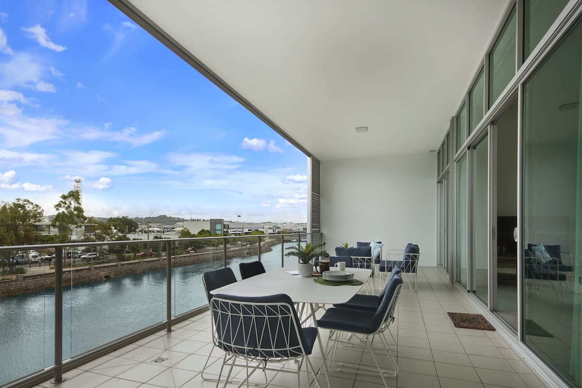 A balcony with a table and chairs, overlooking a river and cityscape.