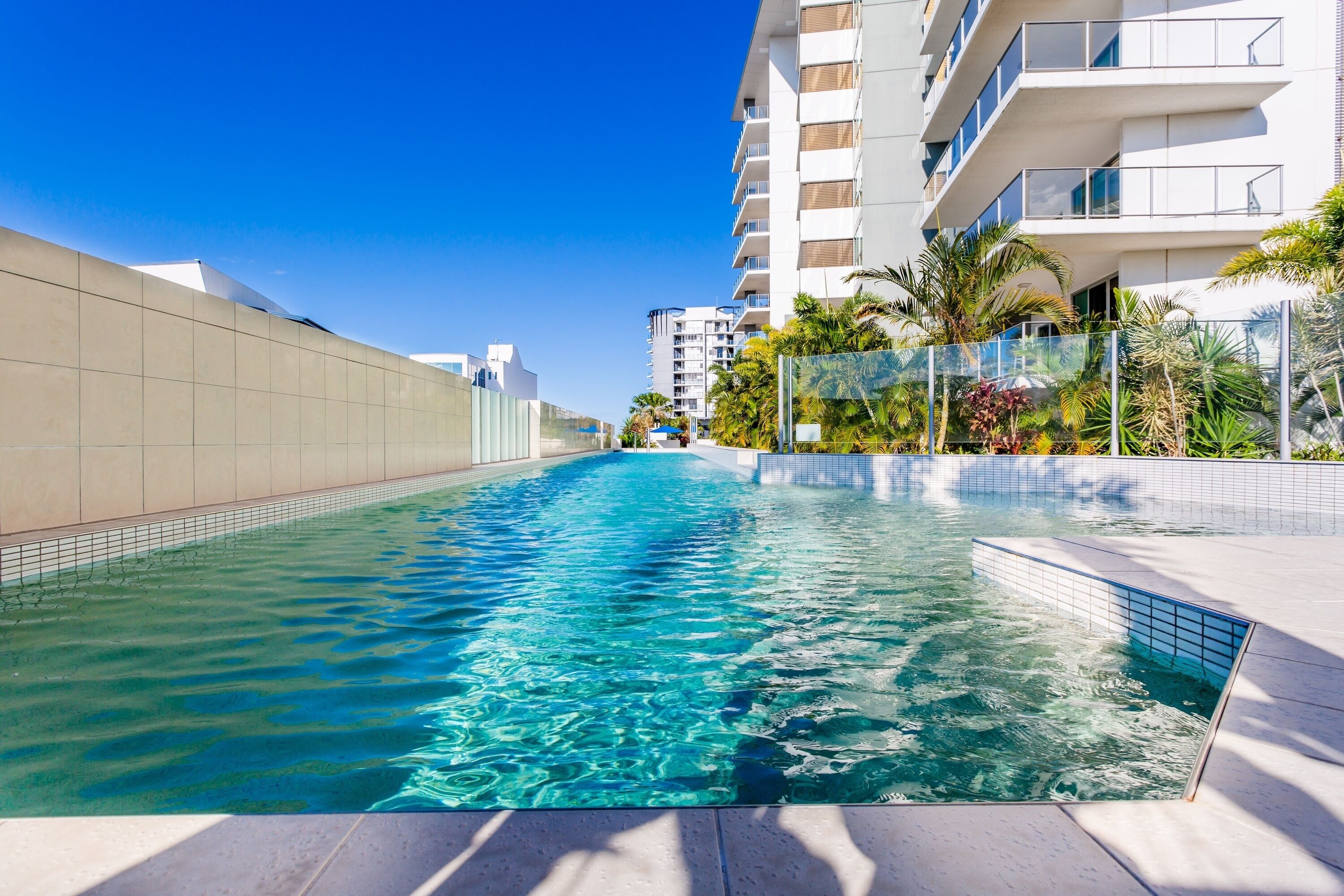 A swimming pool with clear water, surrounded by modern buildings and palm trees.